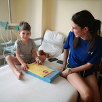 Mały chłopczyk wraz z mamą siedzą na łóżku szpitalnym z upominkiem z okazji Dnia Dziecka.